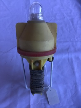 Emergency light in yellow plastic container with a red band. A rope is wound around the bottom stem protected by a metal bracket.