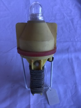 Emergency light in yellow plastic container with a red band. A rope is wound around the bottom stem protected by a metal bracket.