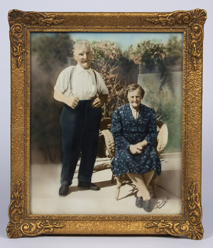 A gold coloured frame contining a colour photograph of an elderly couple called called Alice and Charles Zanoni
