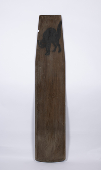 A plank hand modified to be used as a surfboard with a carved and painted cat emblem at the front end.