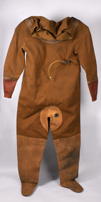  A brown heavy fabric diving suit from the 1950s with rubber and heavier material reinforcement at arms, feet and neck. An air hose attachment can be seen at chest level.