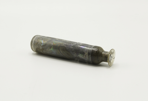 A cylindrical glass bottle containing remains of unknown content with a round neck and no base.