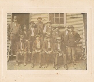 Photograph - GROUP OF TWELVE MEN OUTSIDE CORRUGATED IRON BUILDING