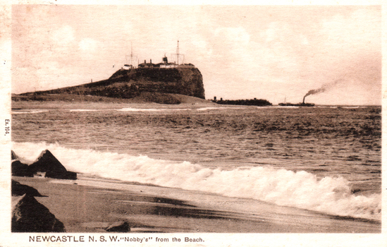 This black-and-white card shows waves breaking on a beach below a coastal headland; on the card is printed “Ex.184. NEWCASTLE N.S.W. ‘Nobby’s’ from the Beach.”
