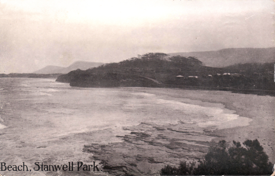 This black-and-white card shows a broad coastal beach backed by wooded hills; on the card is printed “Beach, Stanwell Park.”