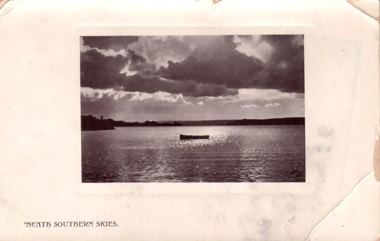This black-and-white card shows a small boat on calm water beneath dramatic clouds; on the card is printed “‘NEATH SOUTHERN SKIES.”