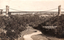 This black-and-white card shows a suspension bridge spanning a wooded river valley; on the card is printed “SUSPENSION Bridge NorthSydney.”