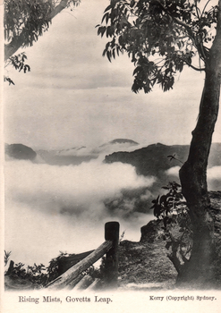 This black-and-white card shows mist rising through a mountainous valley framed by trees; on the card is printed “Rising Mists, Govetts Leap.” and “Kerry (Copyright) Sydney.”