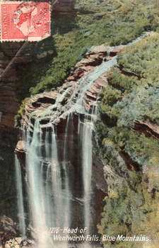 This coloured card shows a waterfall descending over a steep rocky cliff surrounded by bushland; on the card is printed “1276 - Head of Wentworth Falls. Blue Mountains.”
