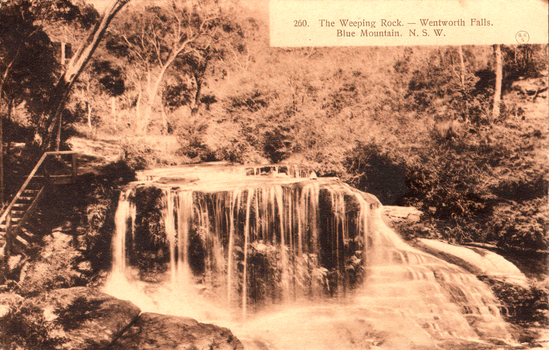 This black-and-white card shows a small waterfall flowing over a broad rock ledge in a wooded setting: On the card is printed “260. The Weeping Rock. — Wentworth Falls. Blue Mountain. N. S. W.”