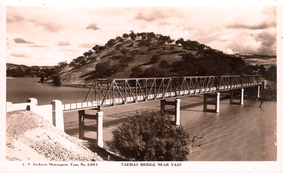 This black-and-white card shows a steel bridge crossing a river below a wooded hillside; on the card is printed “C. V. Jackson, Newsagent, Yass, No. 6803” and “TAEMAS BRIDGE NEAR YASS”.