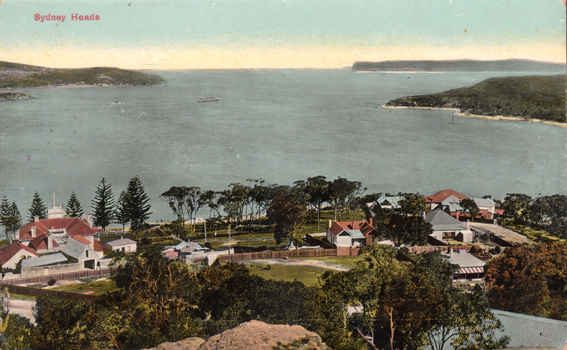This coloured card shows a harbour entrance with houses and trees in the foreground: On the card is printed “Sydney Heads”.
