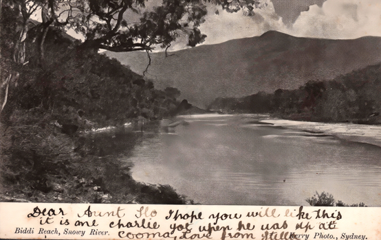 This black-and-white card shows a river winding through a wooded mountain valley: On the card is printed “Biddi Reach, Snowy River. Kerry Photo., Sydney.” The handwriting reads: “Dear Aunt Flo I hope you will like this it is one Charlie got when he was up atCooma. Love from Stella.”