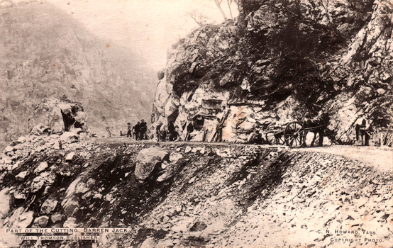 This black-and-white card shows a road cutting through a rocky gorge with people and a horse-drawn cart: On the card is printed “PART OF THE CUTTING, BARREN JACK. WILL THOMSON, PUBLISHER. C. N. HOWARD, YASS. COPYRIGHT PHOTO.”