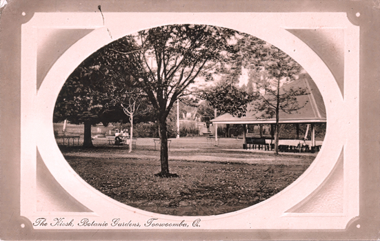 This black-and-white card shows a kiosk among trees in botanical gardens: On the card is printed “The Kiosk, Botanic Gardens, Toowoomba, Q.”