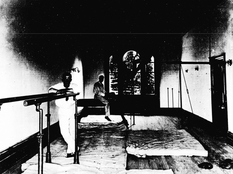 Black and White photo of the Gymnasium, a man standing between the horizontal bars and another behind sitting on the exercise bench