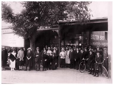An A4 Black and white print of presumably the Boltons Staff outside of their shop in Centre Way Mitchell Street Bendigo possibly in the 1920s, a large group of people and two men with bicycles.