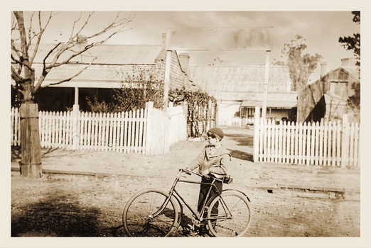Black and White photo of Gordon Glover about 1926 with his bike outside the aerated water factory, the outdated sign over the gateway says: Phillips who was the original factory owner.