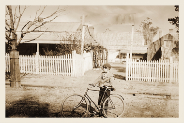 Black and White photo of Gordon Glover about 1926 with his bike outside the aerated water factory, the outdated sign over the gateway says: Phillips who was the original factory owner.