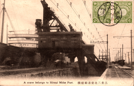 This black-and-white card shows an industrial loading crane beside railway tracks at a port: On the card is printed “A crane belongs to Mitsui Miike Port. The Japanese translates as “Ship-loading crane at Mitsui Miike Port.”