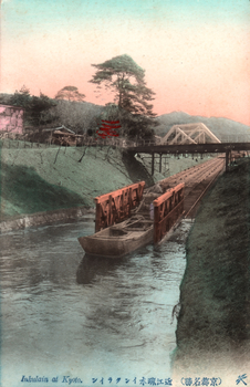 This coloured card shows a boat being carried along a canal incline beneath two bridges. On the card is printed “Inkulain at Kyoto.”.
The Japanese is printed from right to left and reads:
（京都名勝）近江疏水インクライン」 — “Incline on the Ōmi Canal, a famous sight of Kyoto.”