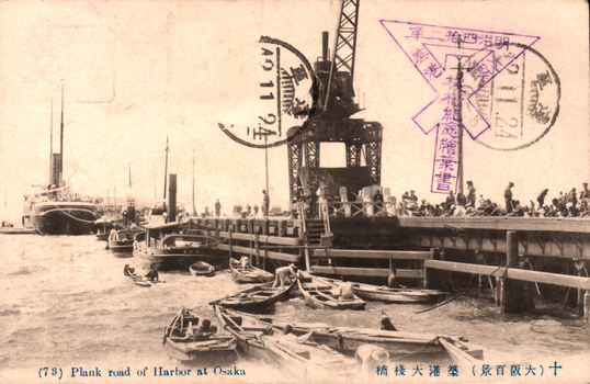 This black-and-white card shows small boats beside a harbour pier with a crane and a steamship. On the card is printed “(73) Plank road of Harbor at Osaka. The Japanese is printed from right to left and reads: 十（大阪百景）築港大桟橋」 — “No. 10, the Great Pier at Osaka Harbour (One Hundred Views of Osaka).”