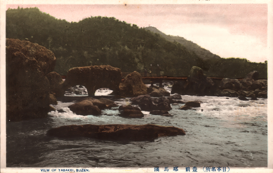 This coloured card shows a rocky river crossed by a low stone bridge, with wooded hills behind. On the card is printed “VIEW OF YABAKEI, BUZEN”. The Japanese is printed from right to left and reads:（日本名所）豊前耶馬溪」 — “Yabakei, Buzen—a famous place in Japan.”