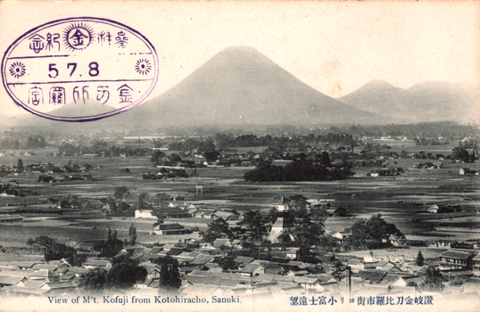 11731.082 This black-and-white card shows a town and fields with a mountain in the background. On the card is printed “View of Mt. Kofuji from Kotohiracho, Sanuki.” The Japanese is printed from right to left and reads 讃岐金刀比羅市街ヨリ小富士遠望, translating as “Distant view of Mount Kofuji from the town of Kotohira, Sanuki.” The Japanese stamp is read mainly from right to left:
参拝記念 — “Commemoration of a visit to the shrine”
金刀比羅宮 — “Kotohira-gū Shrine” or “Konpira Shrine”
The central 金 is the first character of the shrine’s name.
5.7.8 is a date: year 5, seventh month, eighth day; the era name is not shown.