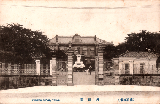 This black-and-white card shows the entrance to a government building behind ornamental gates. On the card is printed “FOREIGN OFFICE, TOKYO”. The Japanese is printed from right to left and reads 外務省（東京百景）, translating as “Foreign Office (One Hundred Views of Tokyo).”