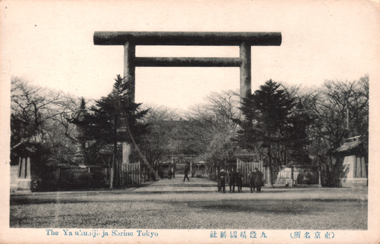 This black-and-white card shows a large torii gate at the entrance to a shrine. On the card is printed “The Yasukunjija Shrine Tokyo". The Japanese is printed from right to left and reads 九段靖國神社（東京名所）, translating as “Yasukuni Shrine at Kudan (a famous place in Tokyo).”