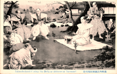 This black-and-white card shows a Japanese samurai seated on a mat during a ceremonial abdomen-cutting scene, surrounded by attendants in a garden. On the card is printed “Takuminokami Cutting The Belly or Abdomen at Tamuratei” The Japanese is printed in the traditional right-to-left direction. Read in modern order, it is:
浅野内匠頭田村邸切腹 English translation: “Asano Takumi-no-kami committing seppuku at the Tamura residence.