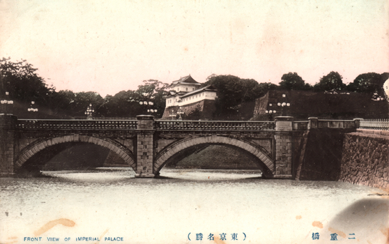 This black-and-white card shows a stone arched bridge across a moat in front of the Imperial Palace grounds. On the card is printed “FRONT VIEW OF IMPERIAL PALACE” The Japanese is printed right-to-left. Read in modern order, it is: 二重橋（東京名勝）English translation: “Nijūbashi (Famous sight of Tokyo).” 二重橋 literally means “Double Bridge.”