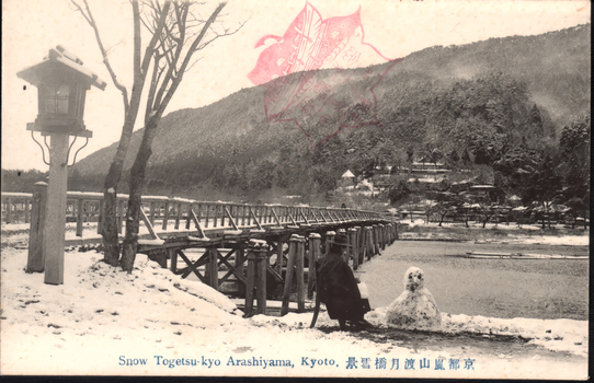 This black-and-white card shows a snow-covered bridge over water with a wooded hillside beyond. On the card is printed “Snow Togetsu-kyo Arashiyama, Kyoto.” The Japanese 京都嵐山渡月橋雪景 translates as “Snow scene of Togetsu Bridge, Arashiyama, Kyoto.”