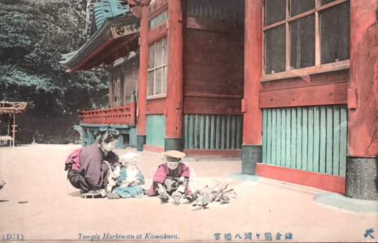 This coloured card shows a woman and two children beside a temple building, with birds on the ground. On the card is printed “(D:1)”, “Temple Hachiman at Kamakura.” The Japanese translates as “Hachiman Shrine at Kamakura” (referring to Tsurugaoka Hachimangū, Kamakura).