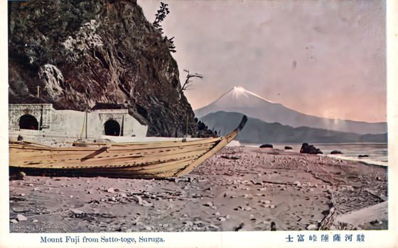 This coloured card shows a boat on a stony shore beside a cliff, with Mount Fuji in the distance. On the card is printed “Mount Fuji from Satto-toge, Suruga.” The Japanese translates as “Mount Fuji from Satta Pass, Suruga.”