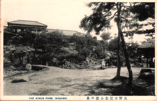 This black-and-white card shows a landscaped park with trees, rocks and buildings on a hillside. On the card is printed “THE KINEN PARK, NAGANO.” and “長野市紀念公園の景”. The Japanese 長野市紀念公園の景 translates as “View of Nagano City Memorial Park.”