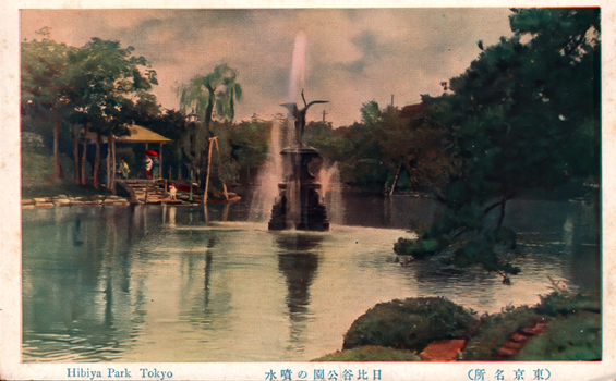 This coloured card shows a pond with a fountain surrounded by trees and garden plantings. On the card is printed “Hibiya Park Tokyo”, “日比谷公園の噴水” and “（東京名所）”. The Japanese translates as:
日比谷公園の噴水 — “The fountain in Hibiya Park”
東京名所 — “Famous places of Tokyo” / “Tokyo sights”