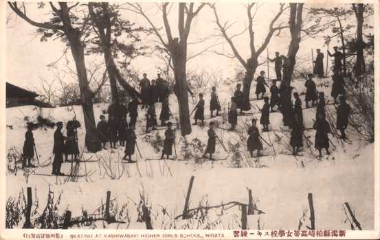 This black-and-white card shows a group of schoolgirls practising in the snow on a wooded slope. On the card is printed “SKATING AT KASHIWASAKI HIGHER GIRLS SCHOOL, NIIGATA” and “新潟縣柏崎高等女學校スキー練習”. The Japanese 新潟縣柏崎高等女學校スキー練習 translates as “Ski practice at Kashiwazaki Higher Girls’ School, Niigata Prefecture.” Notably, the Japanese caption says “ski practice”, although the English caption says “SKATING.”