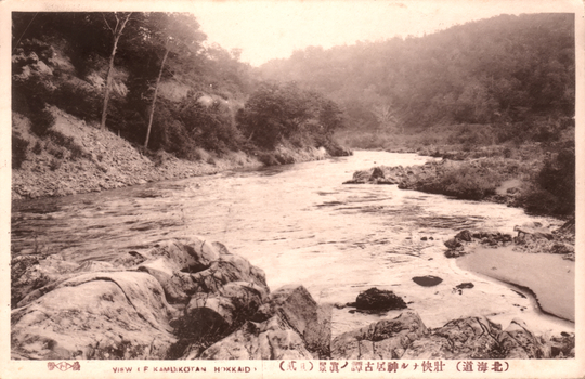This black-and-white card shows a river with rocks and wooded banks. On the card is printed “VIEW I F KAMUIKOTAN HOKKAID...” and “（北海道）壯快ナル神居古潭ノ眞景（其...）”. The Japanese translates in English as “A magnificent view of Kamuikotan, Hokkaidō.” The final bracketed part is unclear