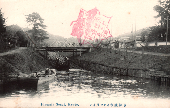 This black-and-white card shows a canal scene with boats, a bridge and buildings. On the card is printed “Inkurain Sosui, Kyoto.” and “京都疏水インクライン”. The Japanese translates in English as “The incline on the Kyoto canal.” More naturally, this means “The Kyoto canal incline.”