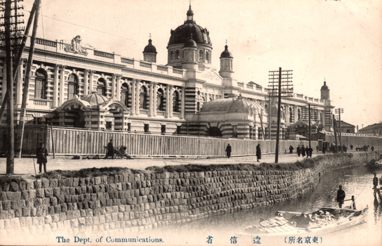 This black-and-white card shows a large government building beside a canal, with pedestrians and boats. On the card is printed “The Dept. of Communications.”, “遞信省” and “（東京名所）”. The Japanese translates as:
遞信省 — “Ministry of Communications”
東京名所 — “Famous places of Tokyo” / “Tokyo sights”