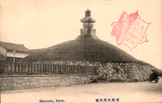 This black-and-white card shows a large burial mound with a stone monument on top. On the card is printed “Mimizuka, Kyoto.” and “京都大佛耳塚”. The Japanese 京都大佛耳塚 translates as “Mimizuka (Ear Mound), Great Buddha, Kyoto.”