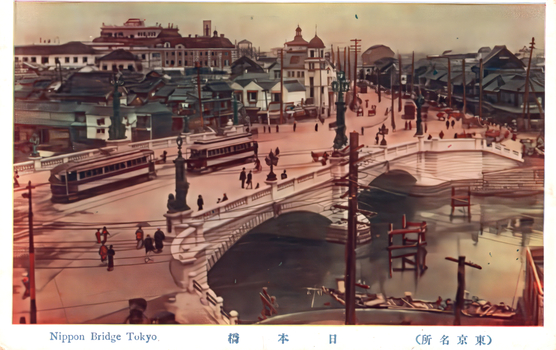 This coloured card shows Nihonbashi bridge with trams, pedestrians, buildings and a canal. On the card is printed “Nippon Bridge Tokyo.”, “日本橋” and “（東京名所）”. The Japanese translates as:
日本橋 — “Nihonbashi” / “Japan Bridge”
東京名所 — “Famous places of Tokyo” / “Tokyo sights”.