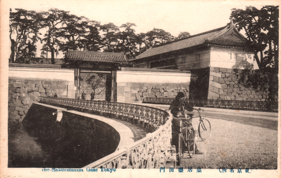 This black-and-white card shows the Sakuradamon Gate and stone walls beside a bridge, with bicycles in the foreground. The English caption is partly obscured; the clearly readable portion is “…Sakuradamon Gate Tokyo”. On the card is also printed “皇居櫻田門” and “（東京名所）”. The Japanese translates as:
皇居櫻田門 — “Sakuradamon Gate of the Imperial Palace”
東京名所 — “Famous places of Tokyo”