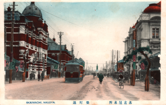 This coloured card shows a broad city street with a tram, pedestrians, cyclists and large commercial buildings. On the card is printed “SKAIMACHI, NAGOYA.”, “栄町通” and “名古屋名所”. The Japanese translates as:
栄町通 — “Sakaemachi Street”
名古屋名所 — “Famous places of Nagoya”