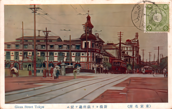 This coloured card shows Ginza Street with tram tracks, trams, pedestrians and large buildings. On the card is printed “Ginza Street Tokyo”, “新橋ヨリ銀座通ヲ望ム” and “（東京名所）”. The Japanese translates as:
新橋ヨリ銀座通ヲ望ム — “View of Ginza Street from Shimbashi”
東京名所 — “Famous places of Tokyo”