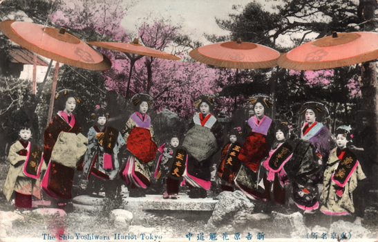 This coloured card shows a group of elaborately dressed women and girls beneath parasols. On the card is printed “The Shin Yoshiwara Harlot Tokyo”, “新吉原花魁道中” and “（東京名所）”. The Japanese translates as:
新吉原花魁道中 — “Procession of the oiran of Shin-Yoshiwara”
東京名所 — “Famous places of Tokyo”