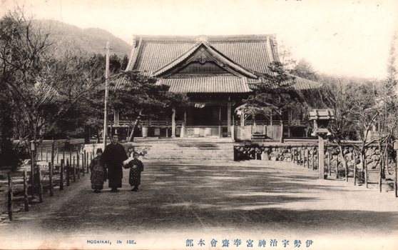 This black-and-white card shows a large shrine or temple building at the end of a broad approach path, with an adult and two children in the foreground. On the card is printed “HOSAIKAI, IN ISE.” and “伊勢神宮奉齋會本部”. The Japanese translates as:
伊勢神宮奉齋會本部 — “Headquarters of the Hōsaikai of Ise Jingū” / “Headquarters of the Ise Shrine devotional association”