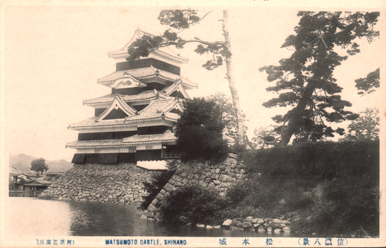 This black-and-white card shows a castle beside a moat and stone embankment. On the card is printed “MATSUMOTO CASTLE, SHINANO.”, “松本城” and “（信濃八景）”. The Japanese translates as:
松本城 — “Matsumoto Castle”
信濃八景 — “Eight Views of Shinano”