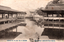 This black-and-white card shows covered corridors and shrine buildings over tidal water, with a torii gate in the distance. On the card is printed “CORRIDOR ON THE. HIGH TIDE AT MIYAZIMA” and “安藝宮島満潮廻廊”. The Japanese translates as:
安藝 — “Aki”
宮島 — “Miyajima”
満潮 — “high tide”
廻廊 — “corridor” / “covered passage”
Together, the Japanese caption means: “Corridor at high tide, Miyajima, Aki.”